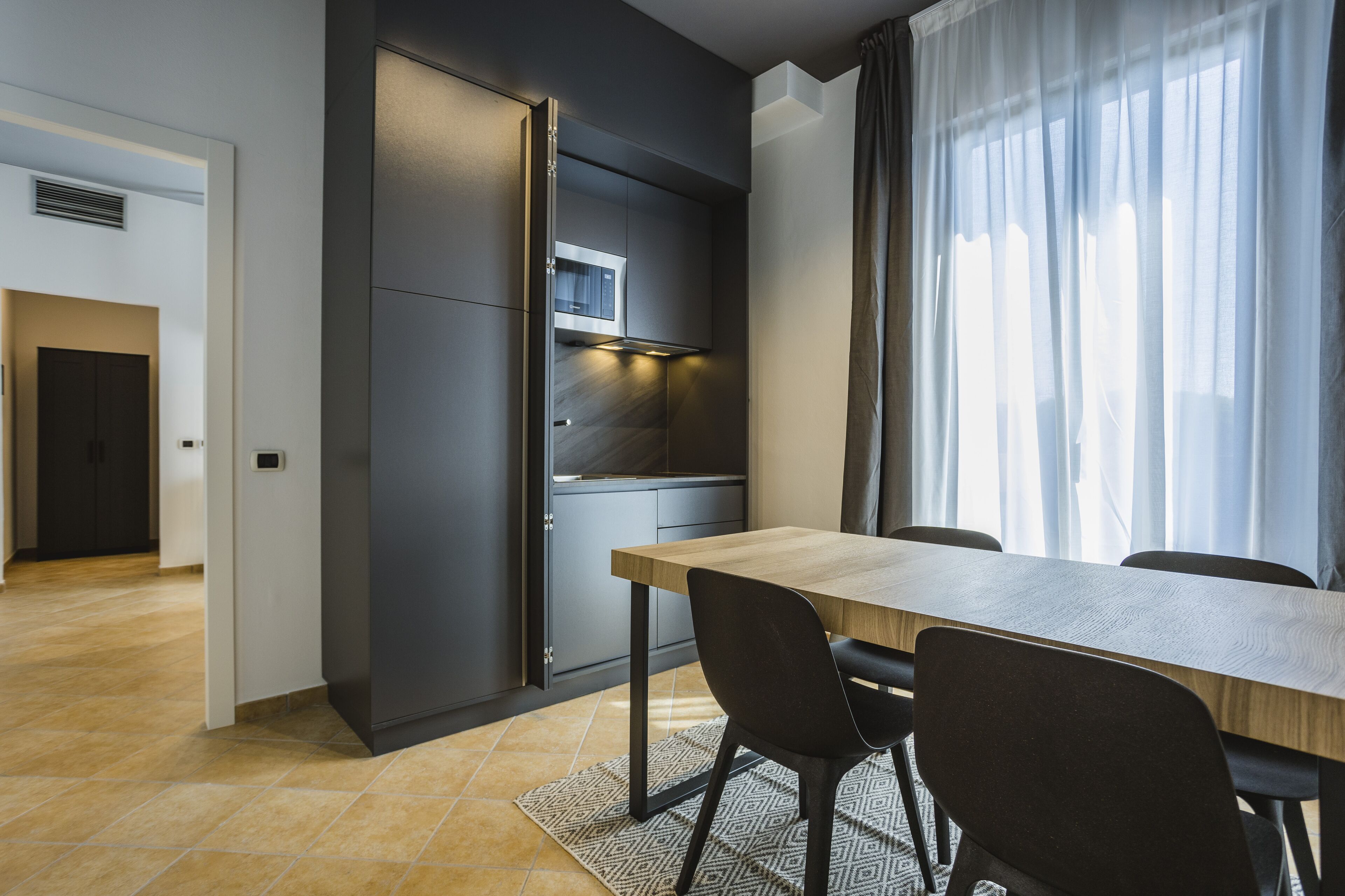 A modern kitchen with a built-in microwave, a dining table with chairs, and a large window with curtains.