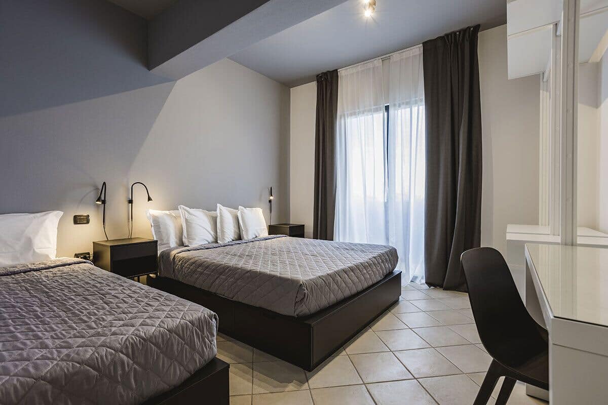 A modern hotel room with two beds, a desk, and a chair.