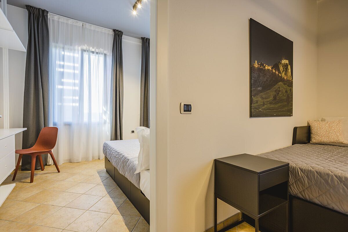 A hotel room with a bed, a desk, a chair, and a painting on the wall.