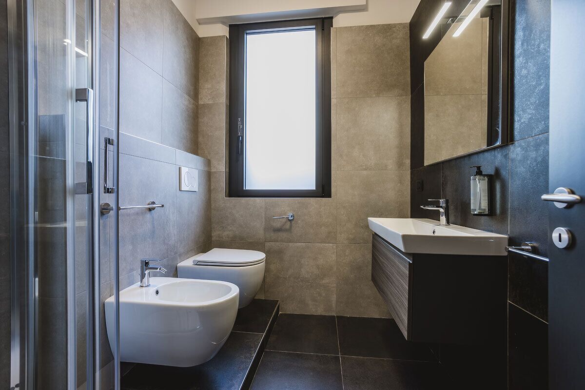 A modern bathroom with a glass shower enclosure, a bidet, a sink, and a large mirror.