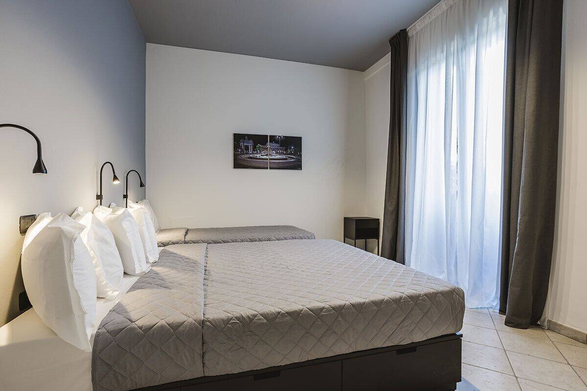 A bedroom with a bed, two bedside lamps, a nightstand, a framed picture on the wall, and a window with curtains.