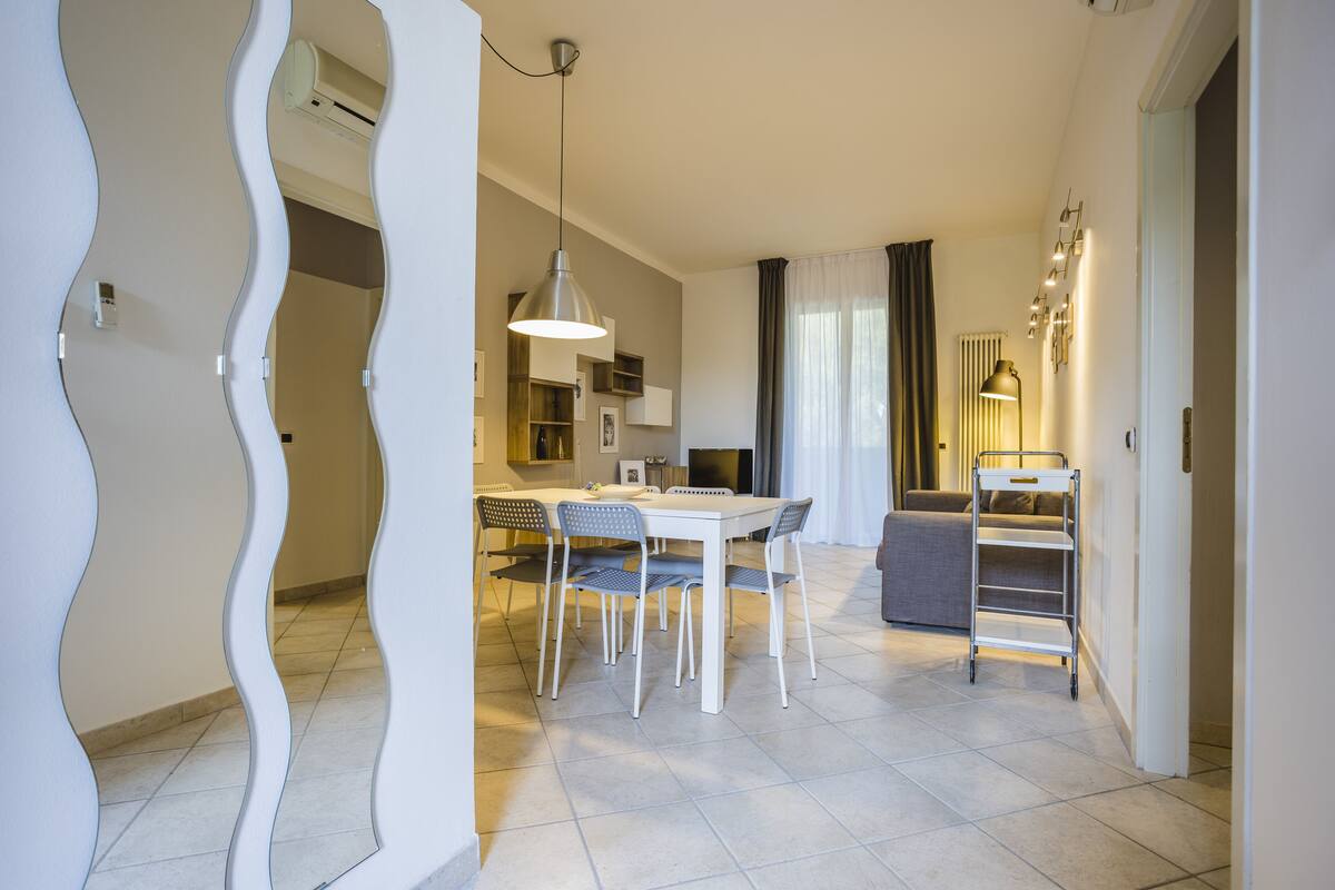 A modern kitchen with white appliances, a dining area with a white table and chairs, and a living area with a sofa and a lamp.