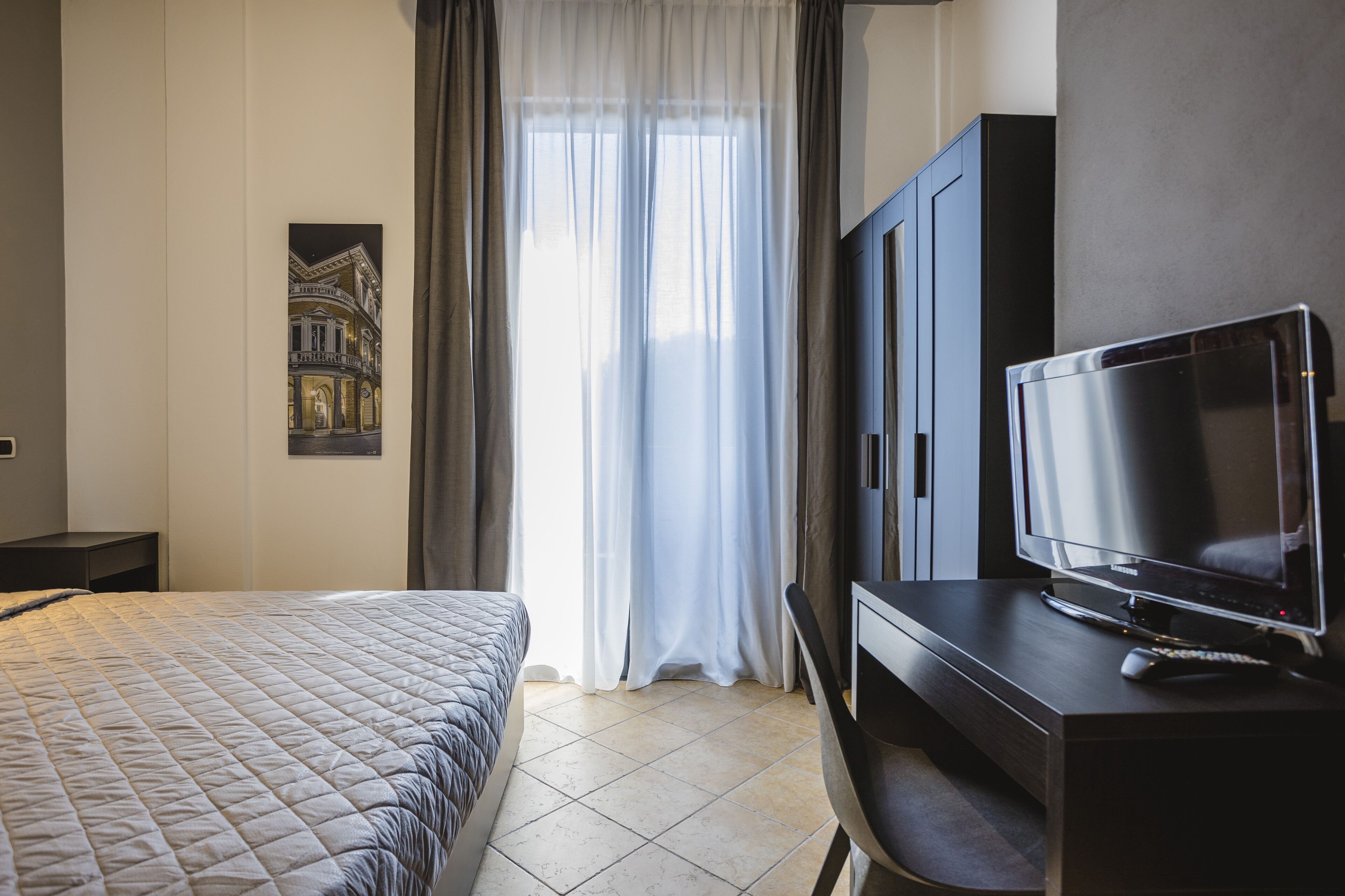 Een hotelkamer met een bed, een televisie op een houten standaard en een schilderij aan de muur.