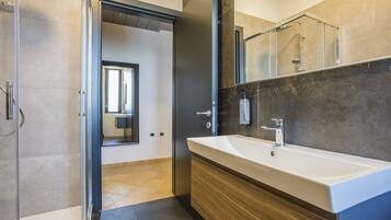 Un bagno moderno con un lavandino ampio, uno specchio e una zona doccia.
