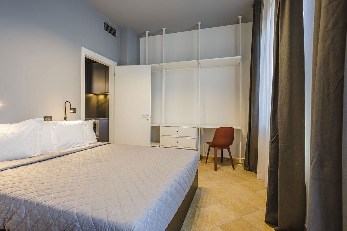 A bedroom with a bed, a desk, a chair, and a wardrobe.