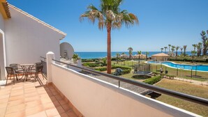 A balcony with a table and chairs, overlooking a pool area with a view of the sea.