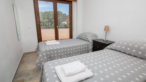 A bedroom with two beds, a nightstand, and a window with a view of trees and buildings.