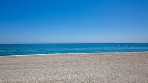 A pebble beach with a clear blue sea and a calm horizon.