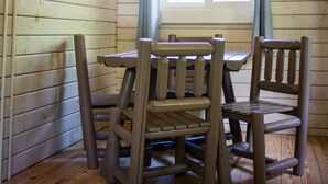 A wooden cabin interior with a dining table and chairs, a window with curtains, and a chimney. - Carowinds Camp Wilderness (Charlotte)