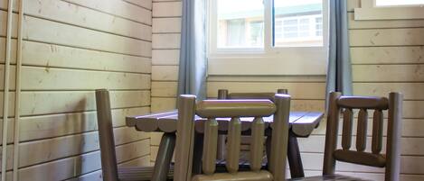 L’intérieur d’un chalet en bois, avec une table et des chaises, une fenêtre avec des rideaux et une cheminée.