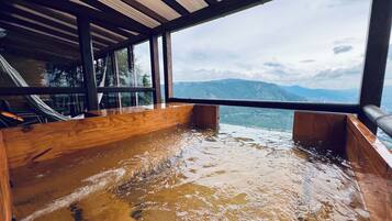 Un jacuzzi de madera con vistas a las montañas a través de amplios ventanales.