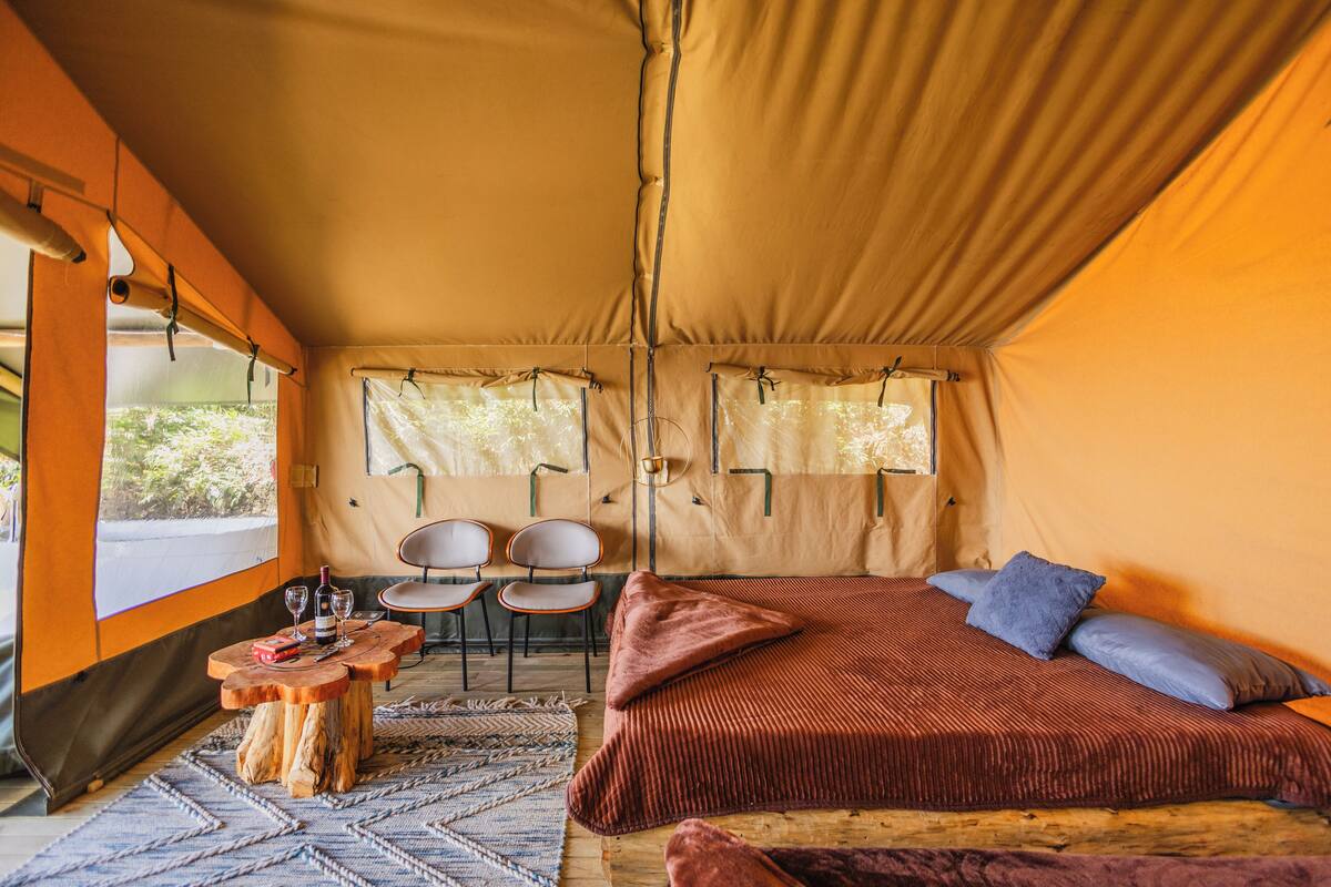A tented room with a bed, a small table with wine glasses, and two chairs.