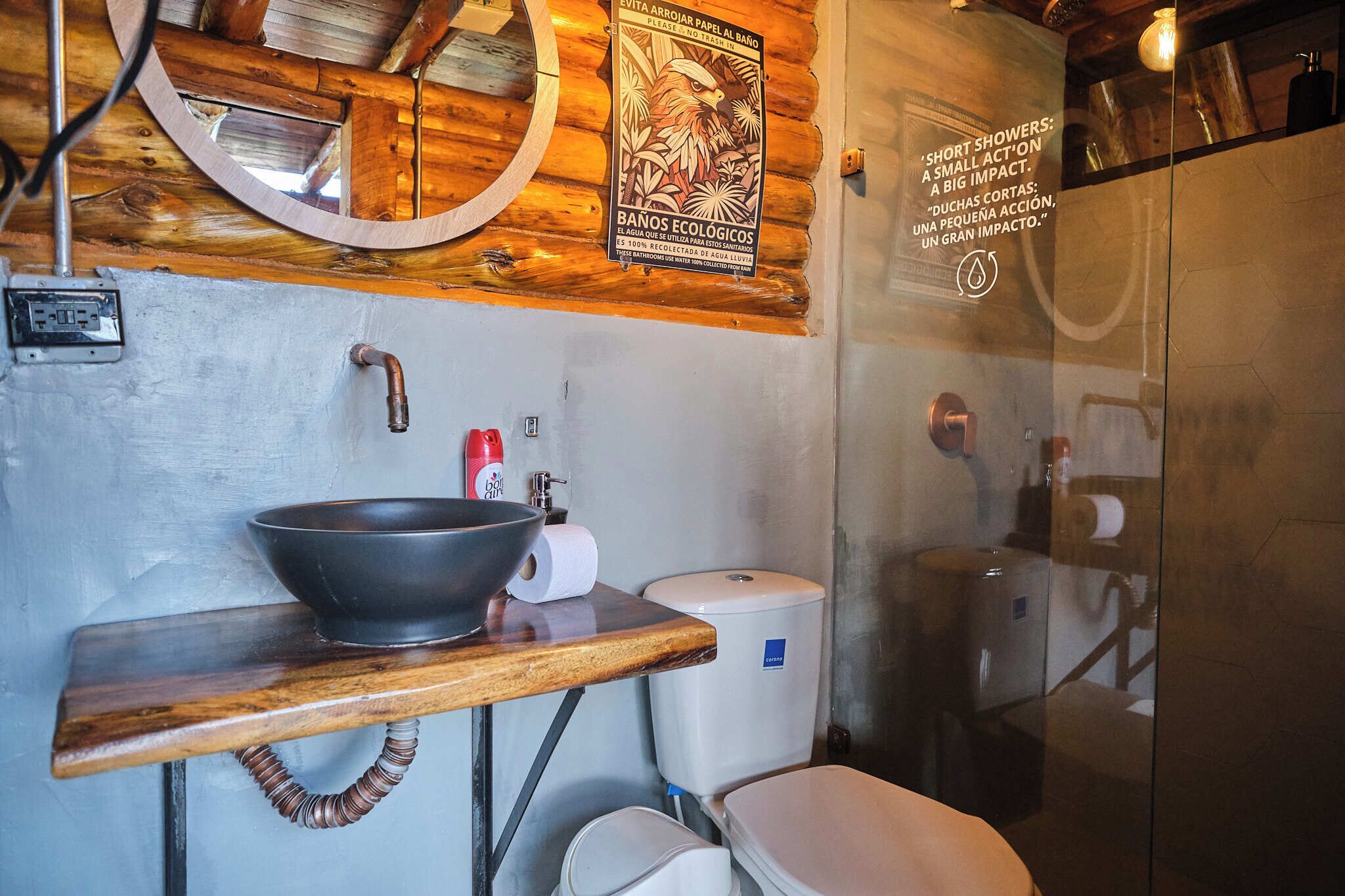 Um banheiro com toucador de madeira, cuba preta, vaso sanitário e área de chuveiro.