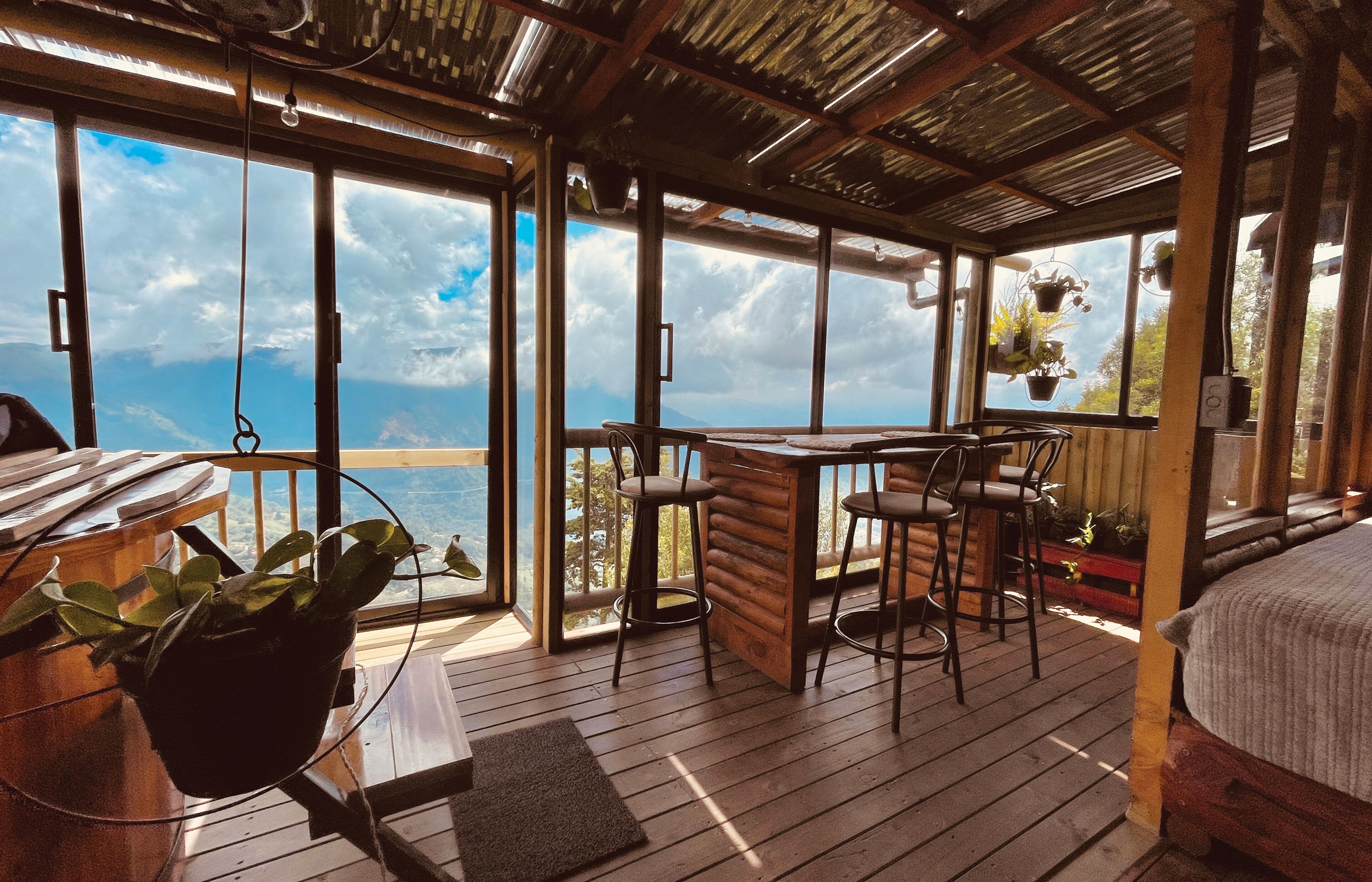 A wooden deck with a table and chairs, large windows with a view of the sea, and hanging plants.