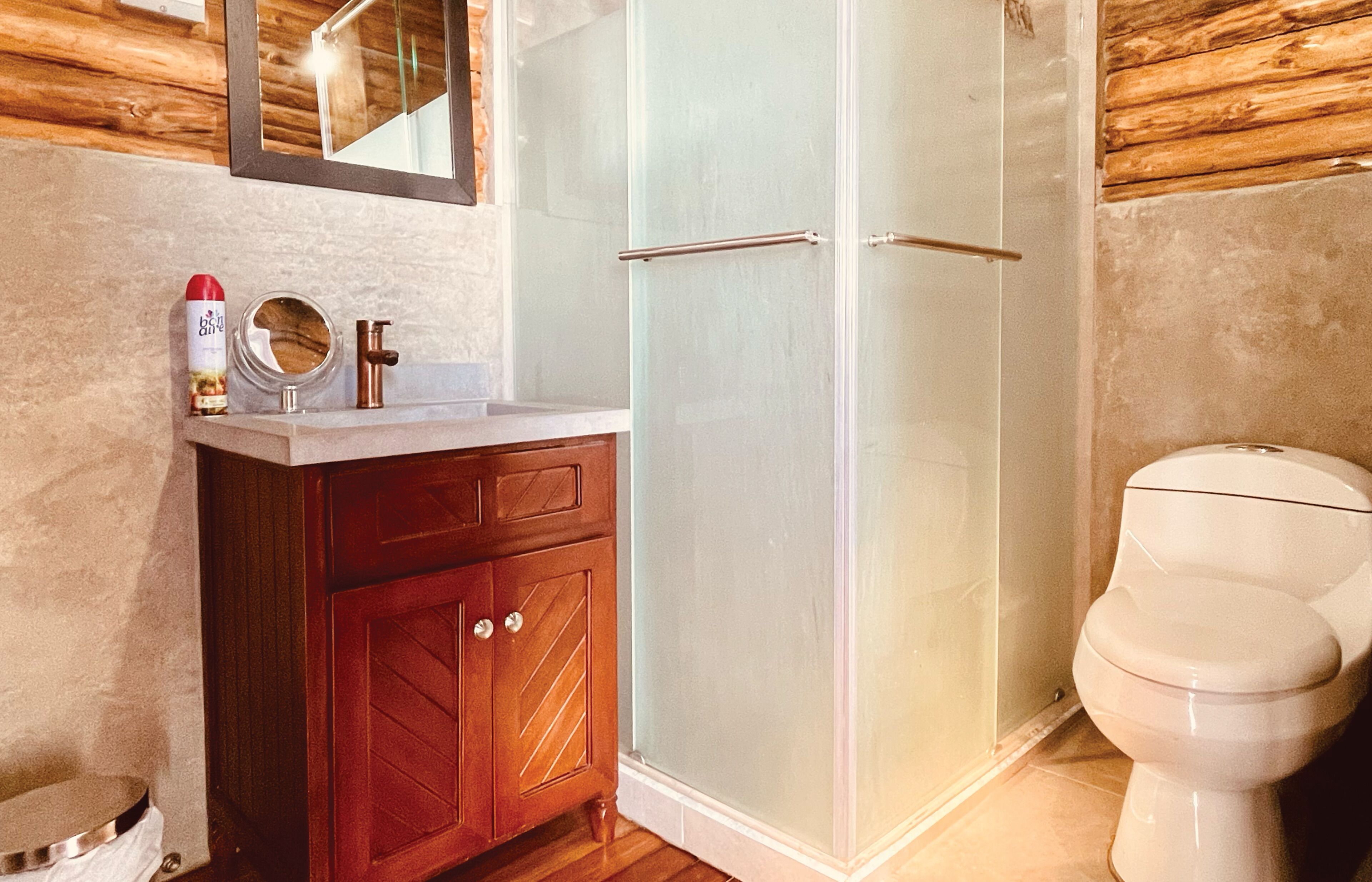 A bathroom with a wooden vanity, a glass shower enclosure, and a white toilet.