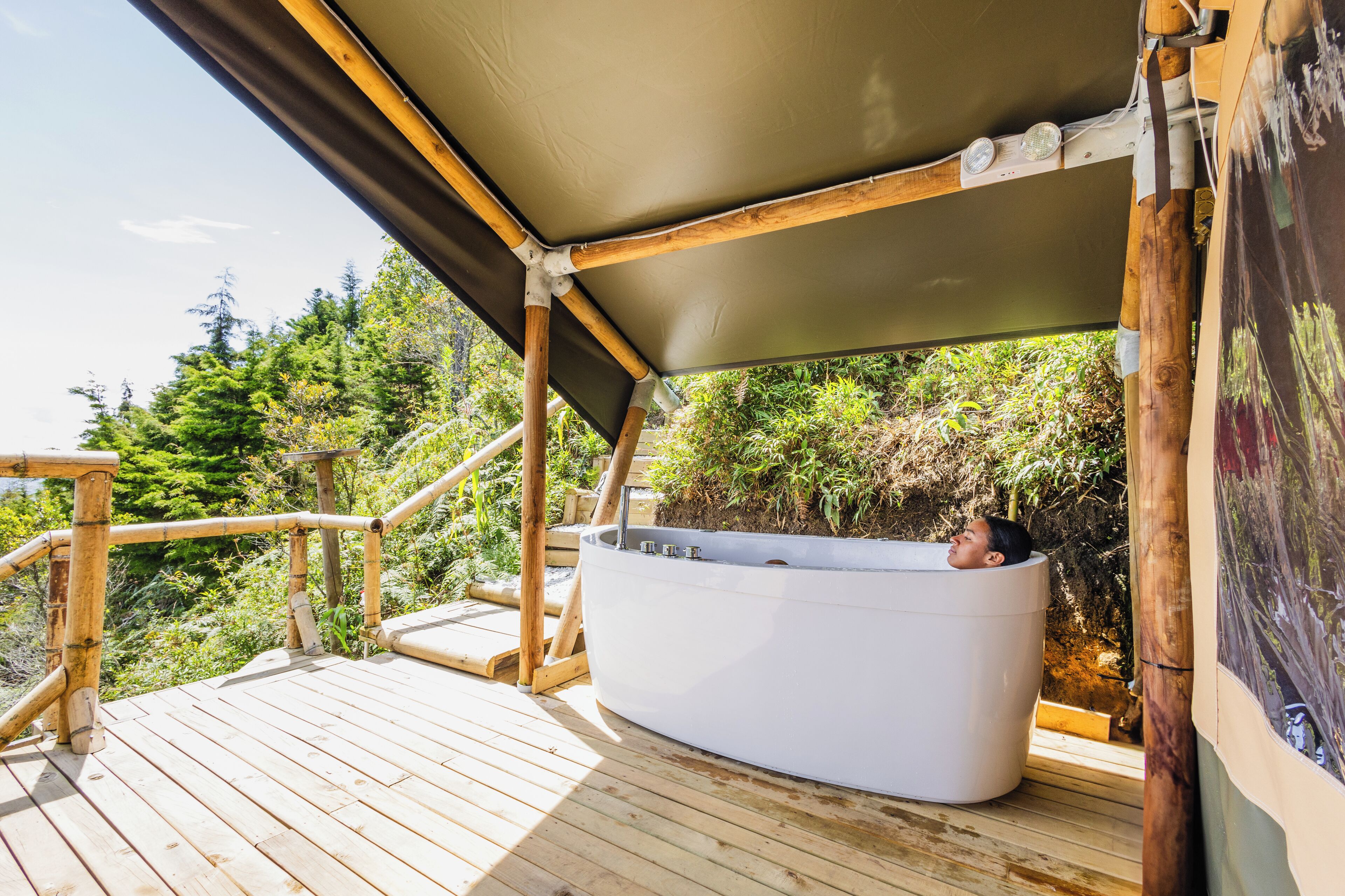 A wooden deck with a hot tub under a shaded area, surrounded by greenery.