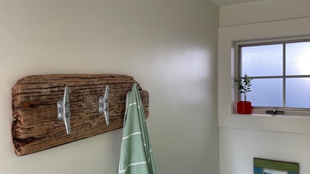 Een rustieke houten kapstok aan de muur, met twee haken en een groen gestreept handdoek er naast.