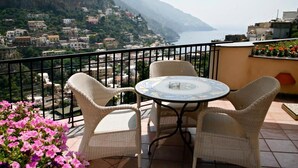 A balcony with wicker chairs and a table, overlooking a coastal town with buildings and a view of the sea. - Splendid Suite with Sea View Terrace  (Positano)