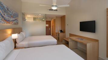 A hotel room with two beds, a desk, a television, and a ceiling fan.