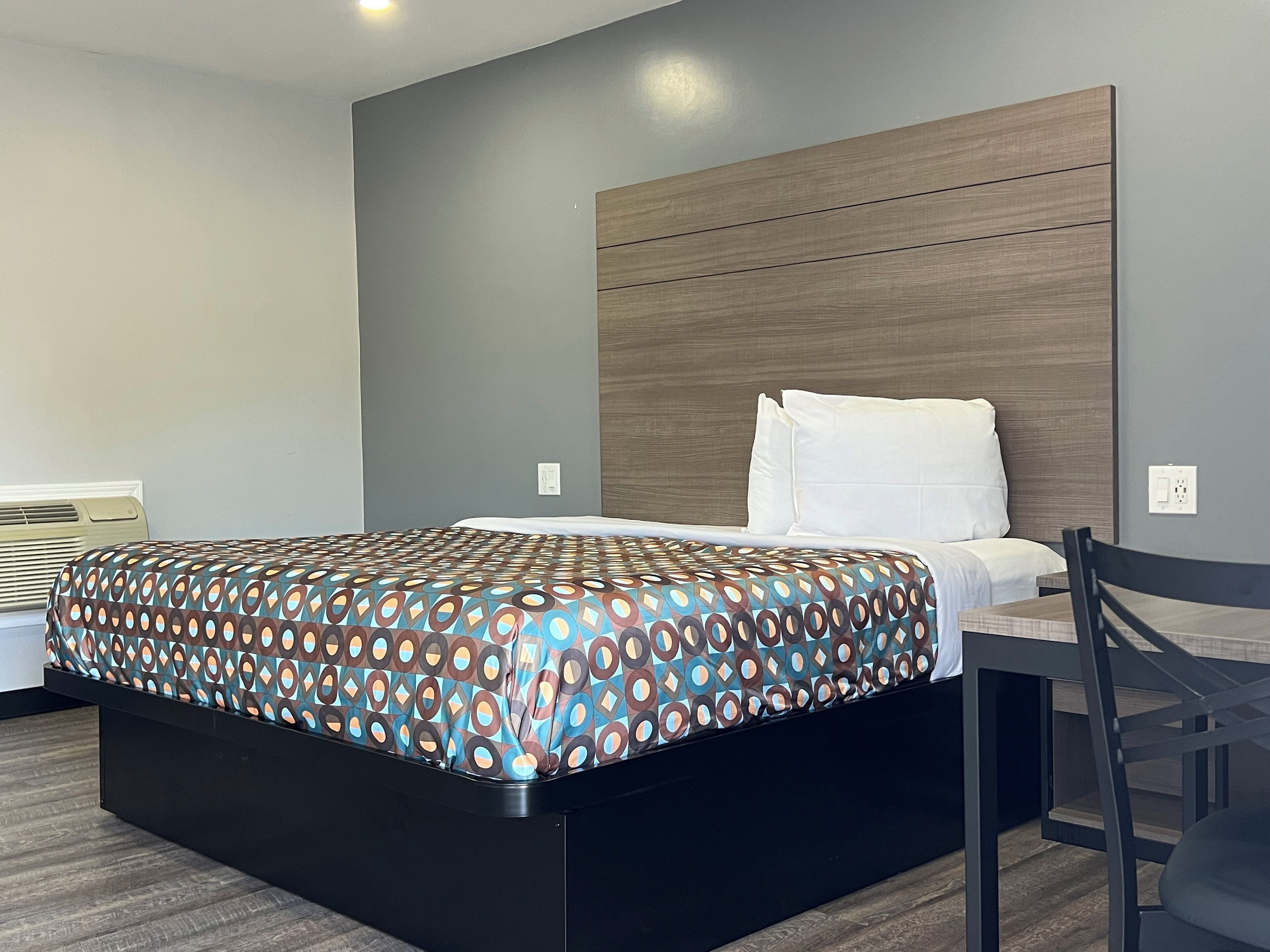 A modern hotel room with a bed, a wooden headboard, a chair, and a desk.