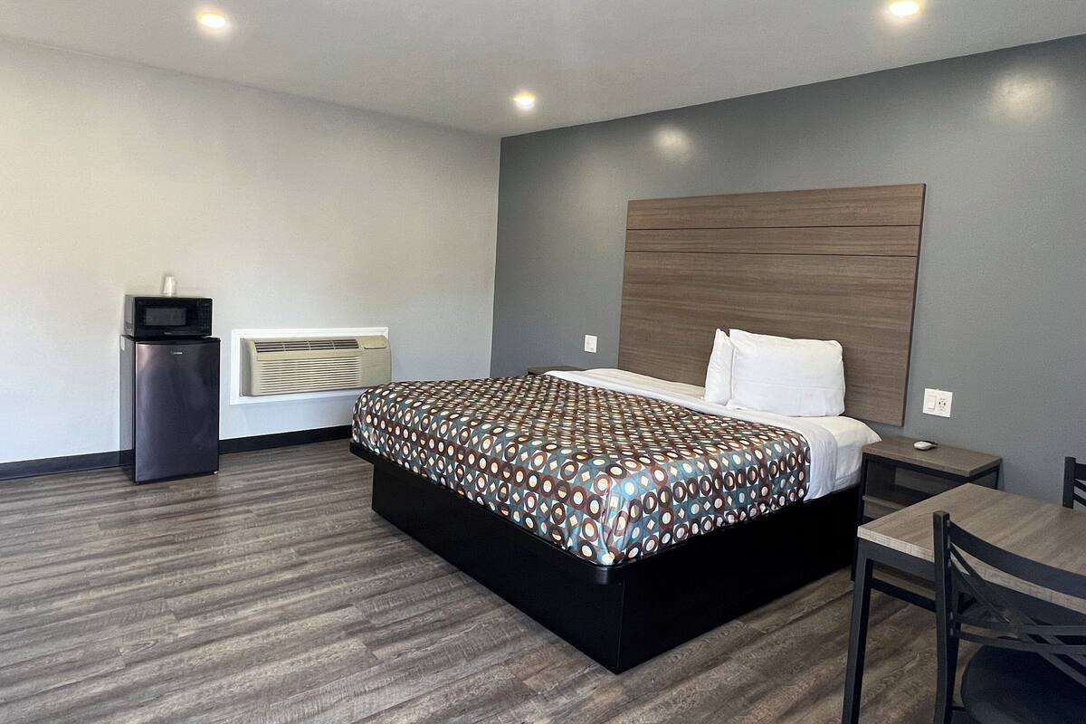 Quarto de hotel com cama, escrivaninha, cadeira, micro-ondas e aquecedor.