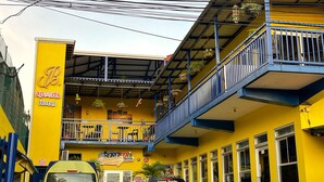 Un edificio amarillo con balcón azul, un letrero que dice 'apairts Hotel', y dos coches estacionados.