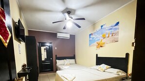 Habitación de hotel con cama, escritorio, silla, ventilador de techo y pared decorada con cuadros.