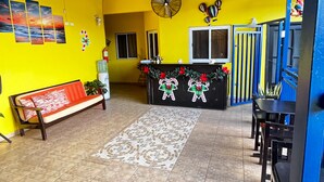 Una habitación con una pared amarilla, un banco, una recepción decorada para las fiestas, un ventilador y una ventana.
