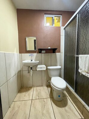A small bathroom with a toilet, sink, and a shower area. - B. Apart Hotel (Roatan)
