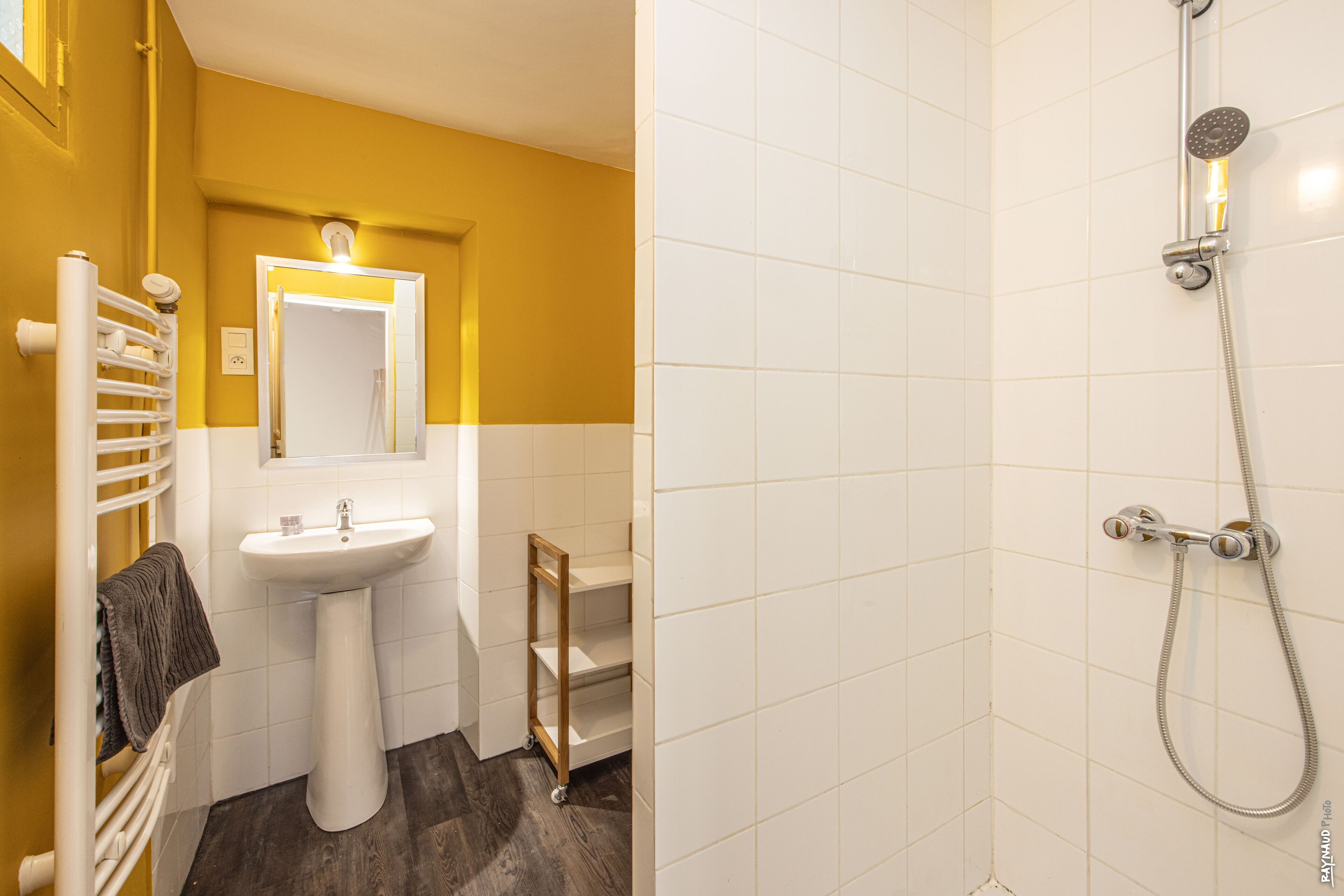 Un baño con un lavamanos blanco, un espejo, un perchero para toallas y una ducha con cabezal de ducha de mano.