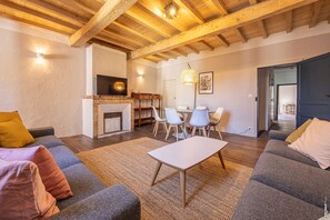 A spacious living room with a fireplace, a dining area with a table and chairs, and a modern kitchen with wooden beams. - Maison 116 - Hypercentre - Gaillac (Gaillac)
