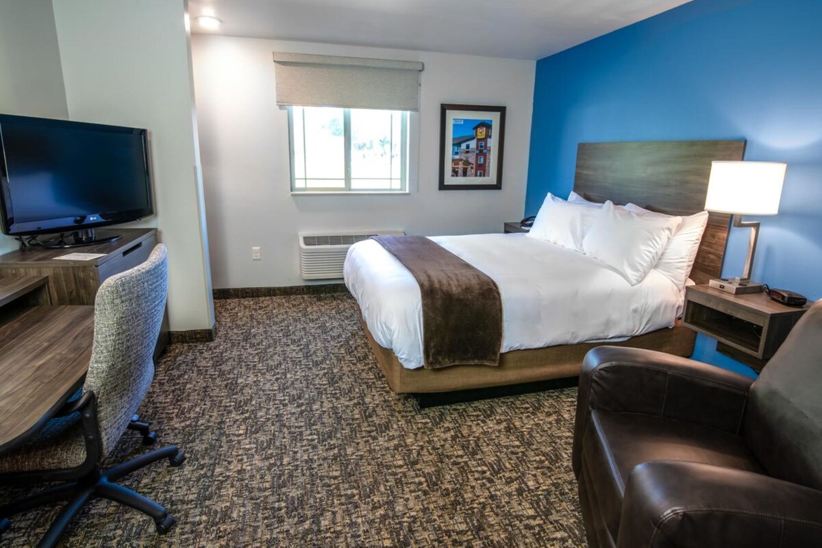 A hotel room with a bed, a desk with a computer, a chair, a TV, and a window.