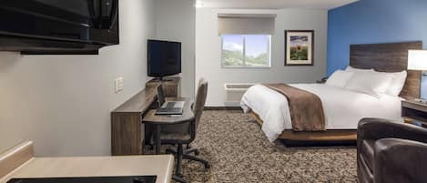 A hotel room with a bed, desk, chair, TV, and a view of the outdoors.