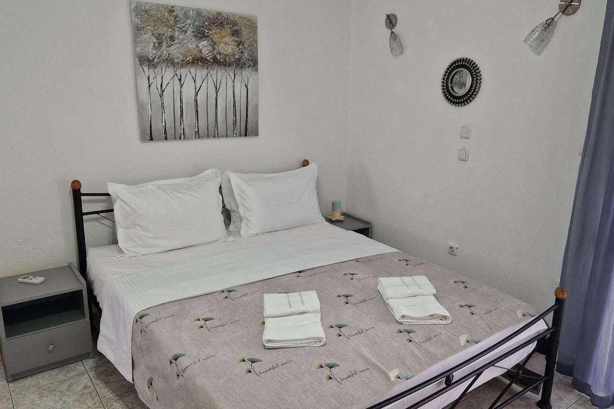 A neatly made bed with white linens and a floral-patterned duvet, a bedside table with a lamp, and a wall-mounted artwork.