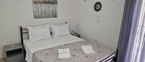 A neatly made bed with white linens and a floral-patterned duvet, a bedside table with a lamp, and a wall-mounted artwork.