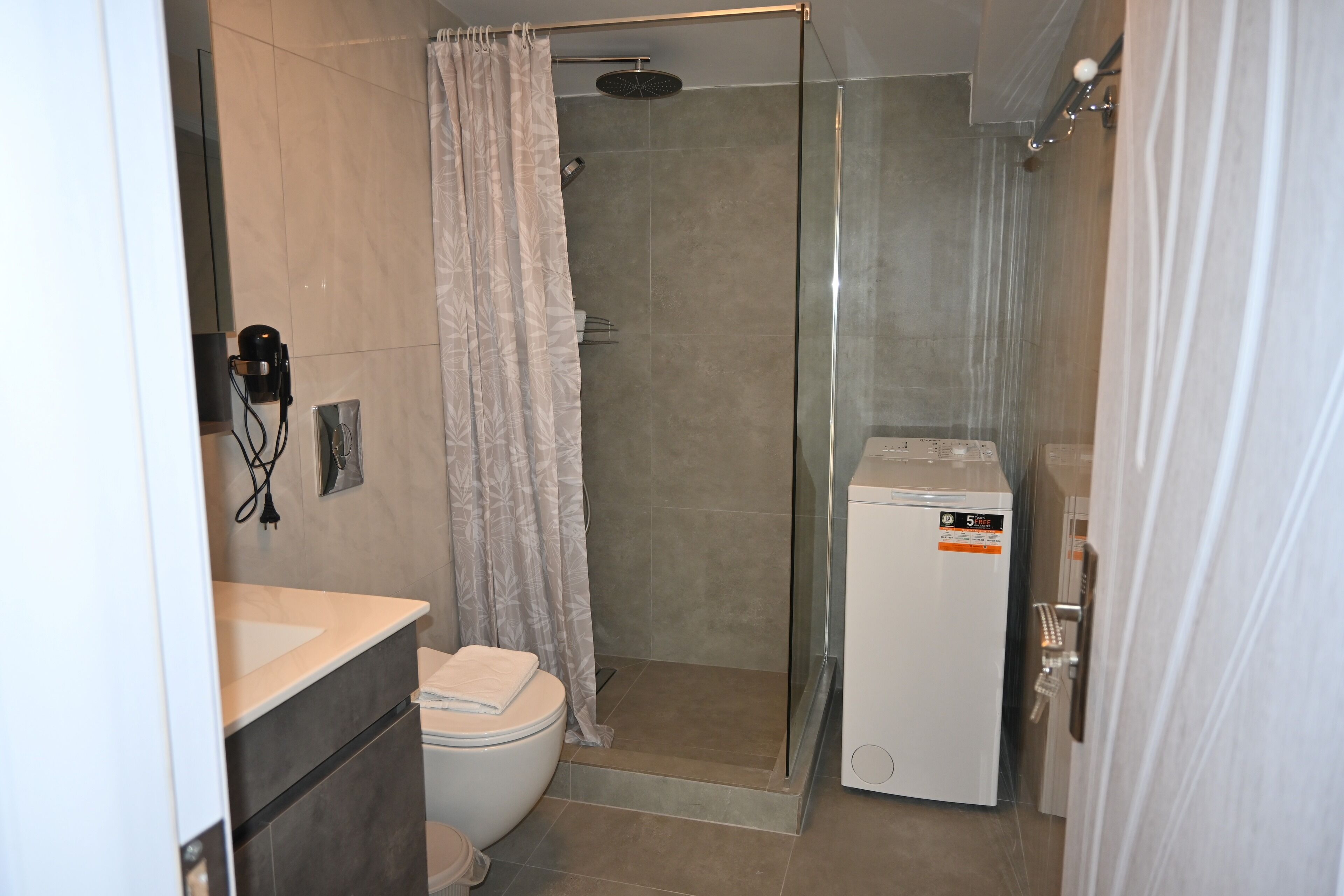 Un baño con ducha, inodoro y un refrigerador pequeño.