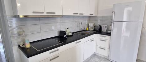 A modern kitchen with white cabinets, black countertops, and a white refrigerator.