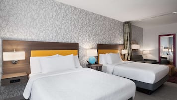 Habitació d'hotel amb dos llits, cadascun amb capçalera de fusta i roba de llit blanca. Hi ha taules de nit amb làmpades i un mirall a una paret.