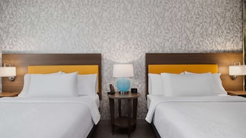 Habitación de hotel con dos camas, cada una con cabecero de madera y ropa de cama blanca. Entre las camas, una pequeña mesa con una lámpara y un globo decorativo.