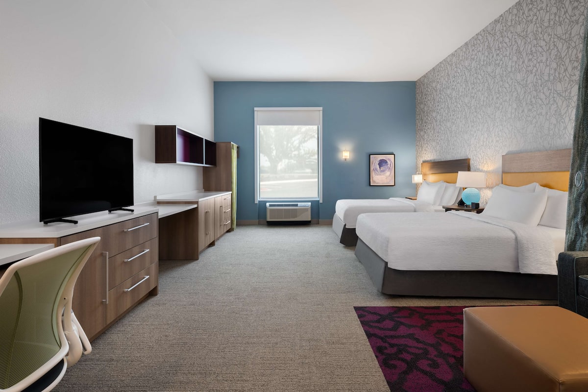 Habitación de hotel con televisión, escritorio, dos camas y un ventanal grande.