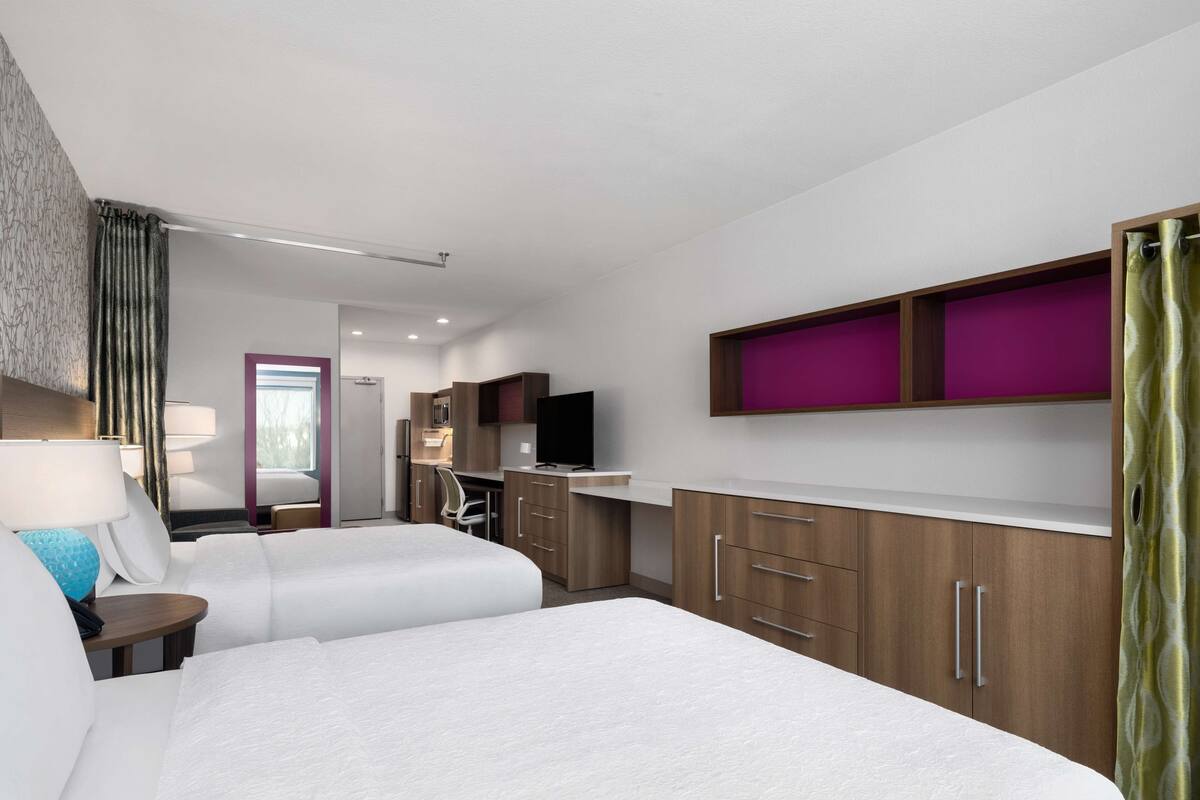 Una habitación de hotel con dos camas, un escritorio, un televisor y un minibar.