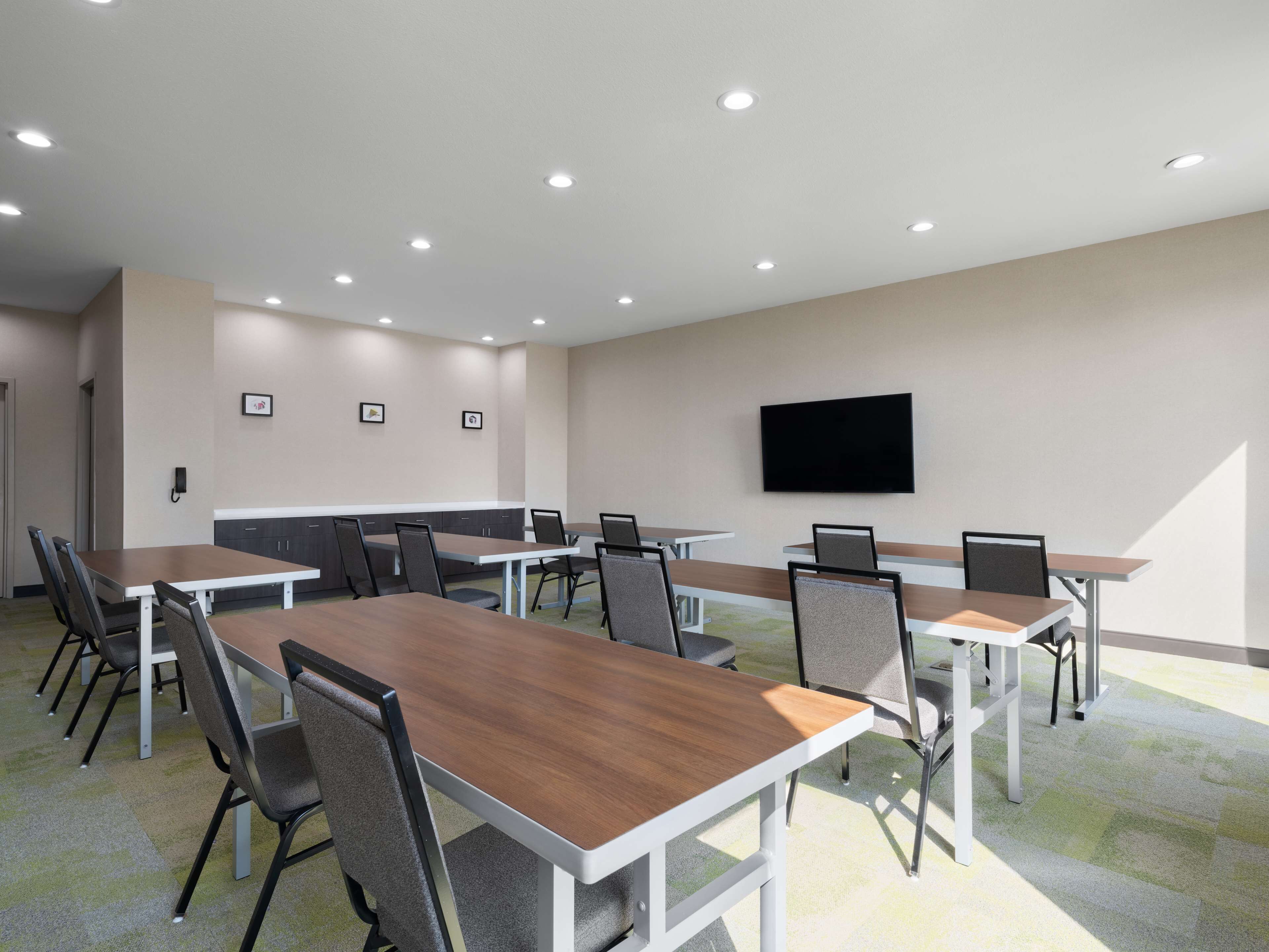 A conference room with multiple tables and chairs, a flat-screen TV mounted on the wall, and recessed ceiling lights.