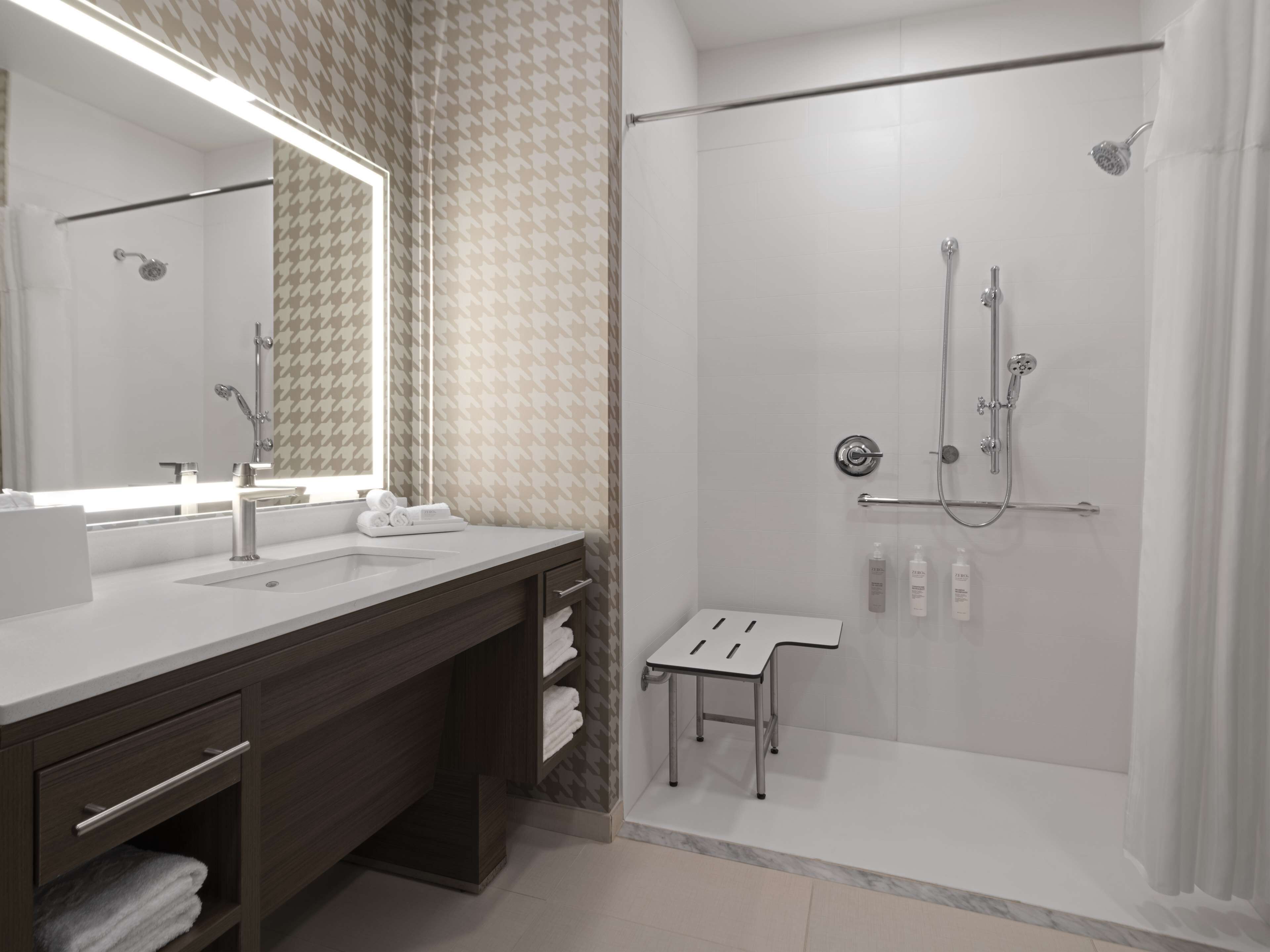 Un baño moderno con un espejo grande, dos lavamanos, una ducha y una mesita.