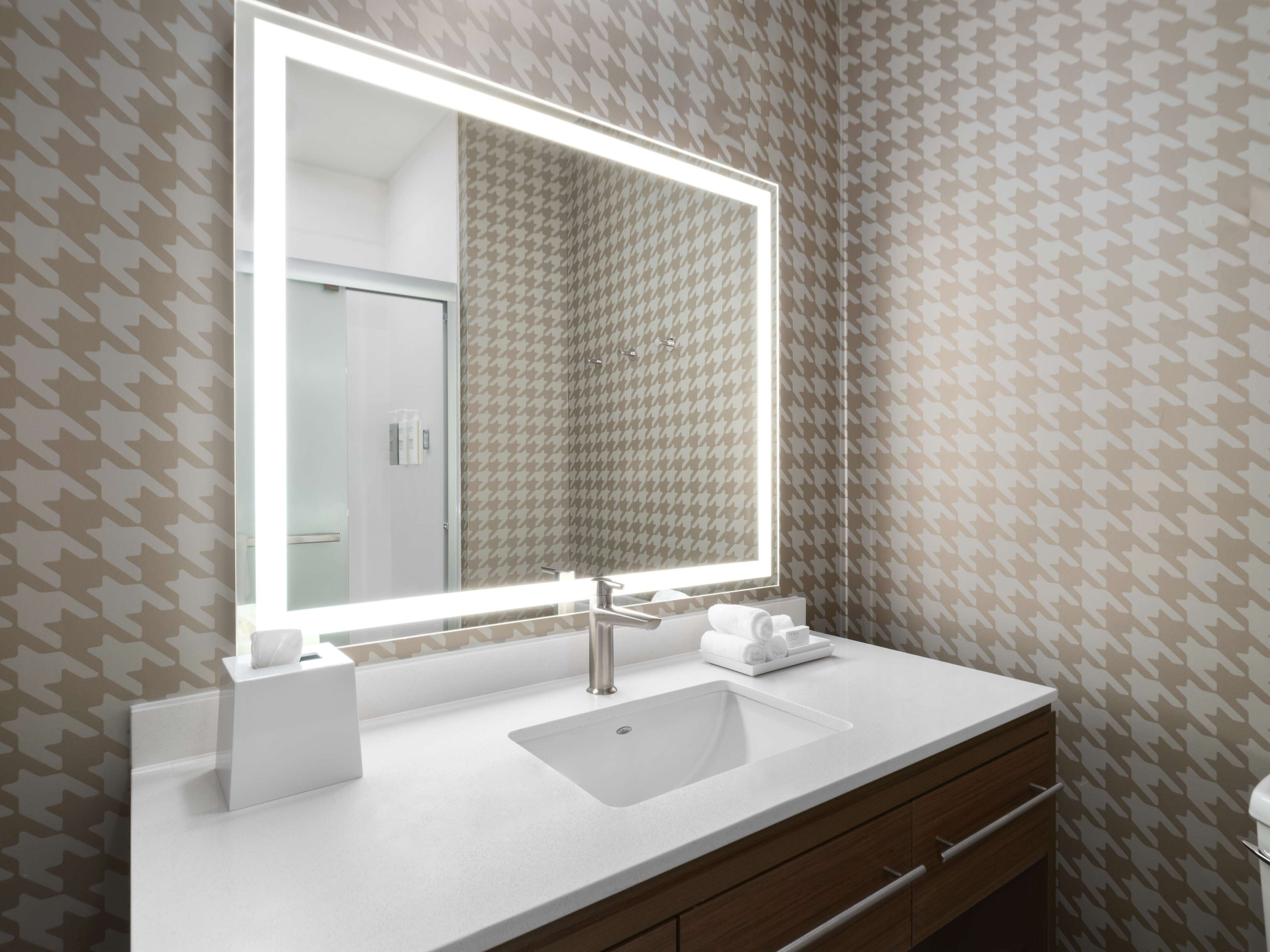 A bathroom with a large mirror, white sink, and wooden vanity.