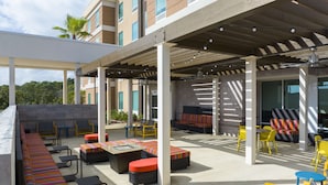 Un patio al aire libre con espacios de estar, incluyendo sofás y sillas, y una zona cubierta con ventilador de techo.