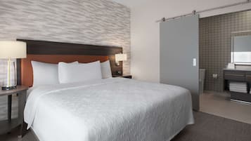 A hotel room with a large bed, a nightstand with a lamp, a bathroom with a mirror and towel rack.