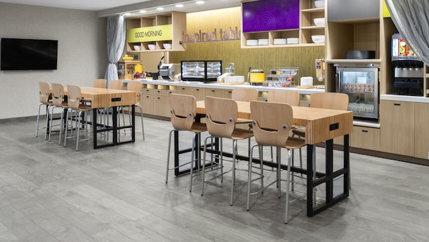 Un café moderno con mesas y sillas de madera, una barra con una máquina de café y un refrigerador.