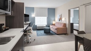 Una habitación de hotel moderna con kitchenette, un sofá, un escritorio y un ventanal grande.