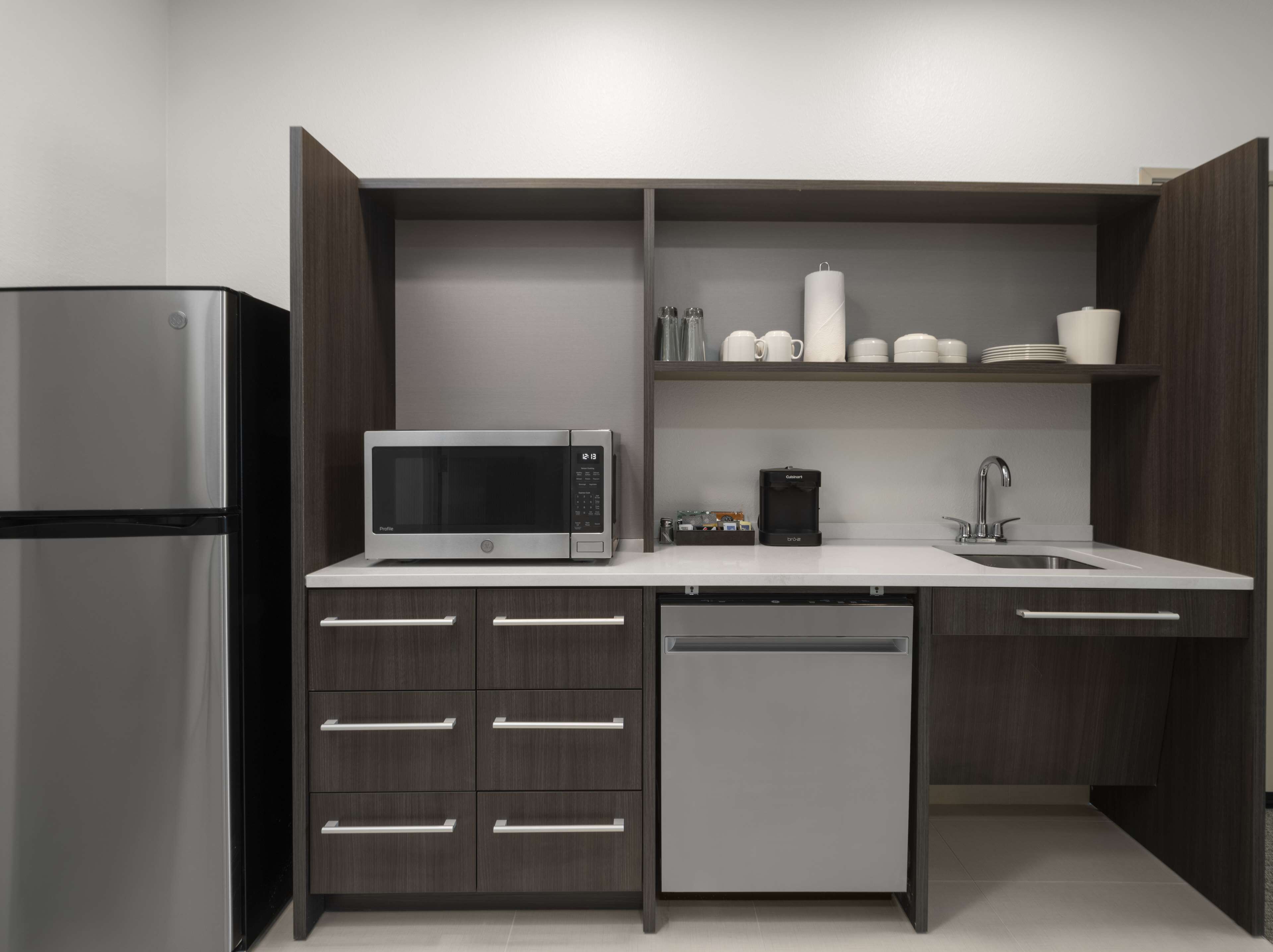A modern kitchen with a stainless steel refrigerator, a built-in microwave, a coffee maker, and a dishwasher.