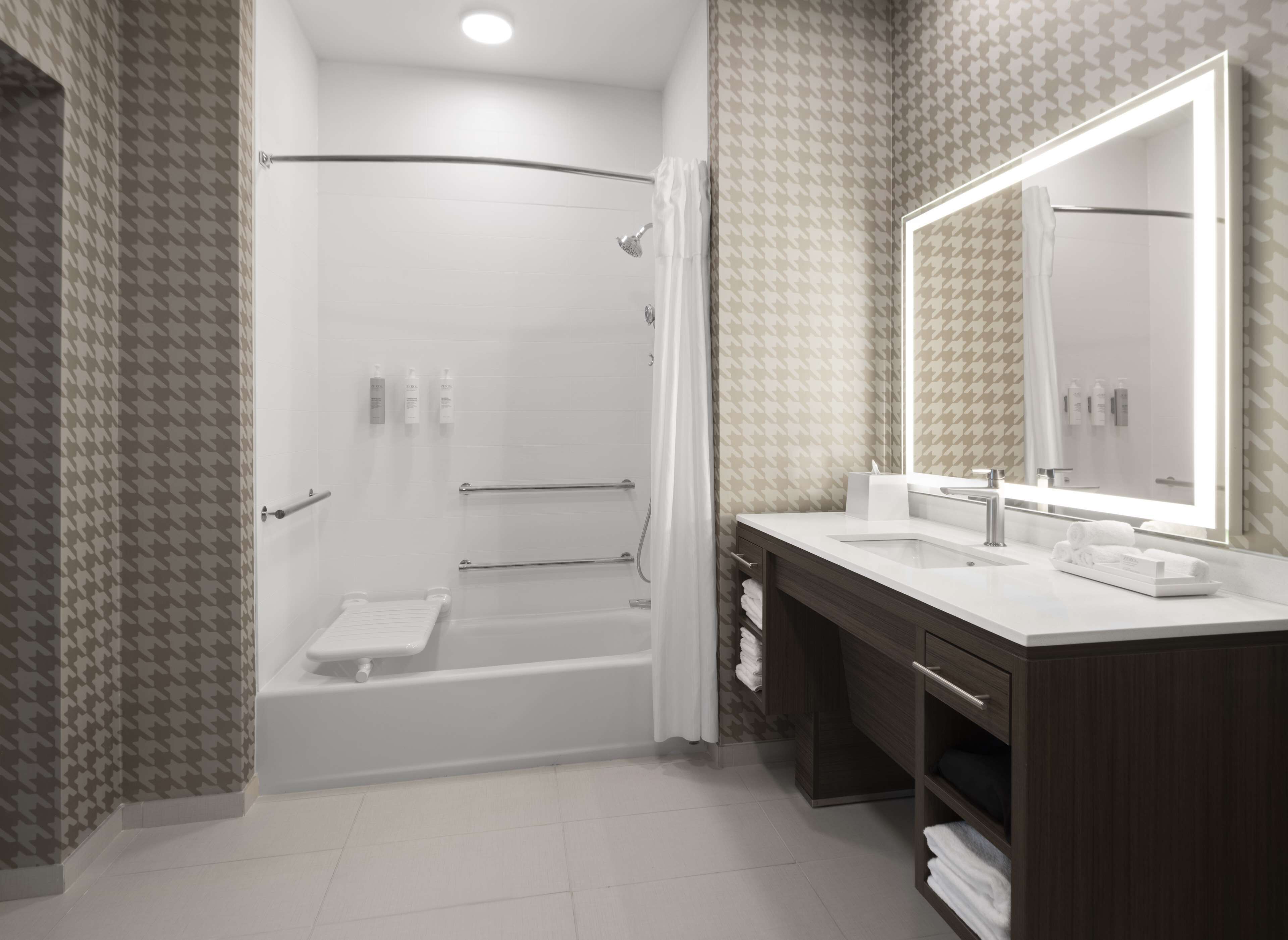 Een moderne badkamer met een douche, bad, wastafel met grote spiegel en handdoekrek.